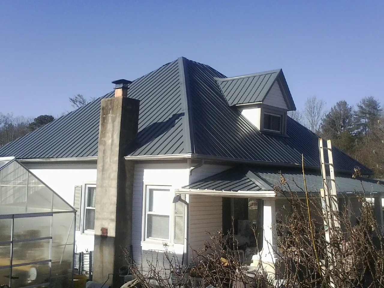 Dark blue standing seam metal roof on a white farmhouse with dormer — Slate & Tile Roof Repair by Roofing Brothers in Lulu