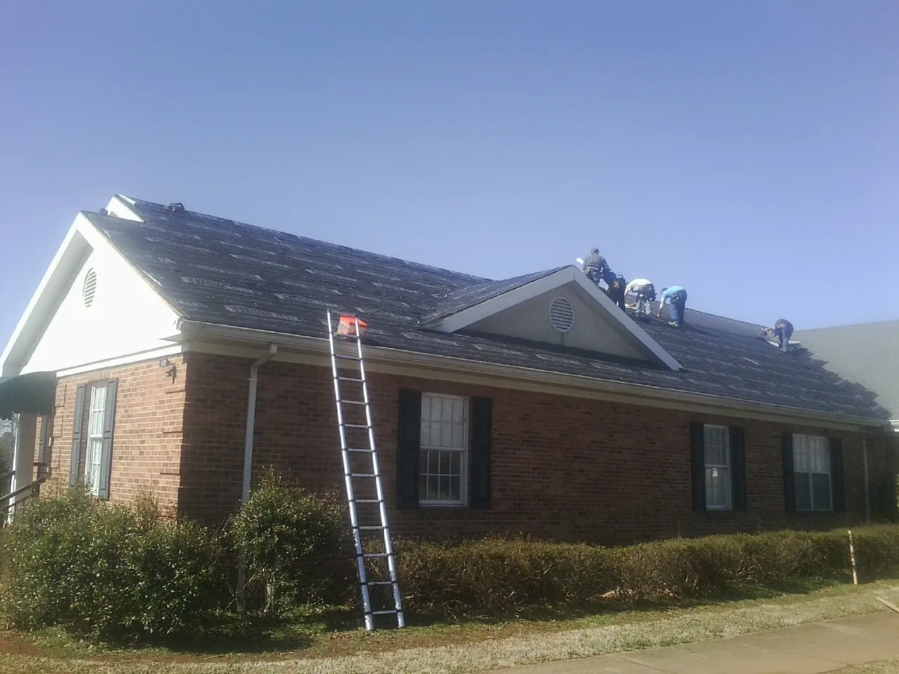 Crew tearing shingles off a brick ranch roof with a ladder set — Emergency Roof Repair work by our crew in Lulu