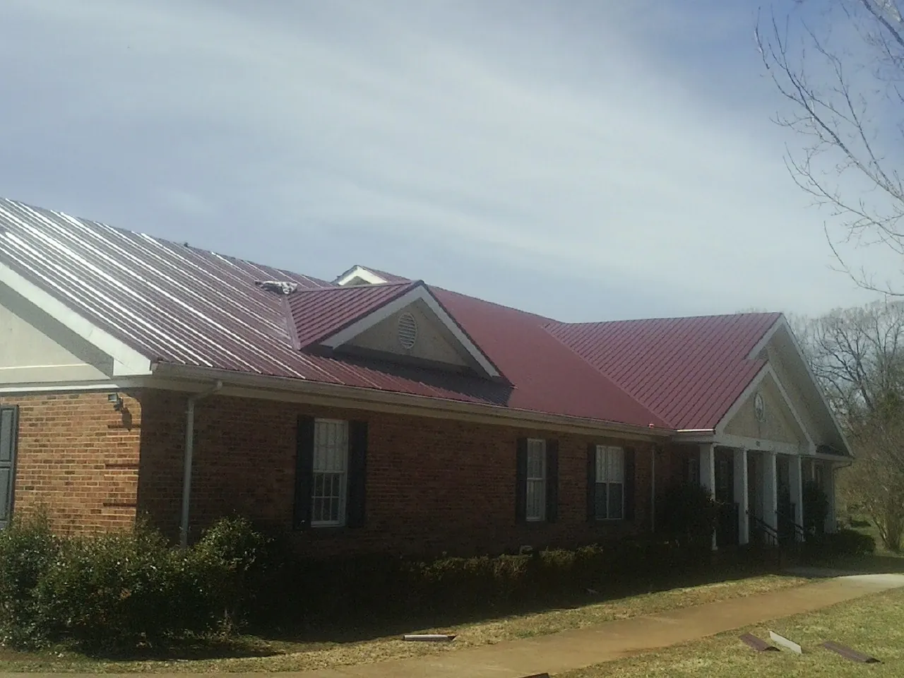 Red metal roof with gabled entries on a long brick building, from a Hail Damage Roof Repair job in Lulu
