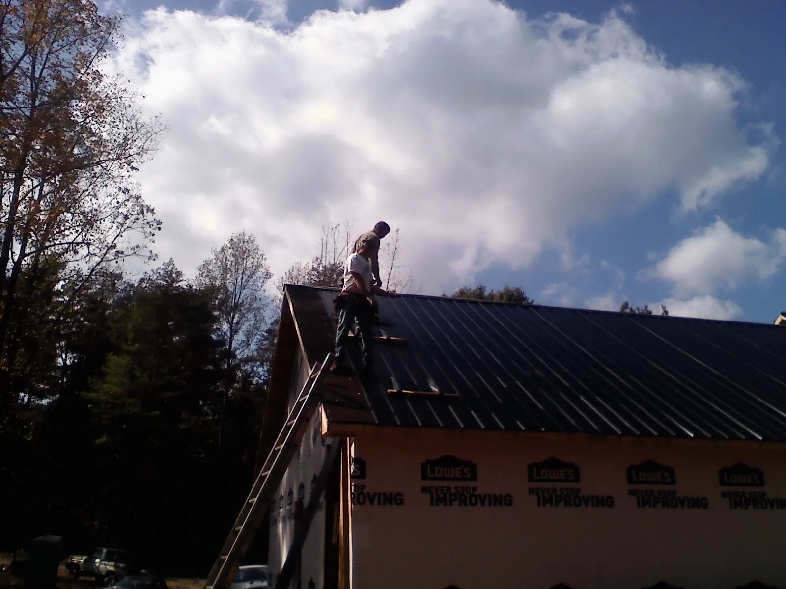 Roofer fastening dark metal panels high against a cloudy sky, from a Roof Inspection job in Lulu